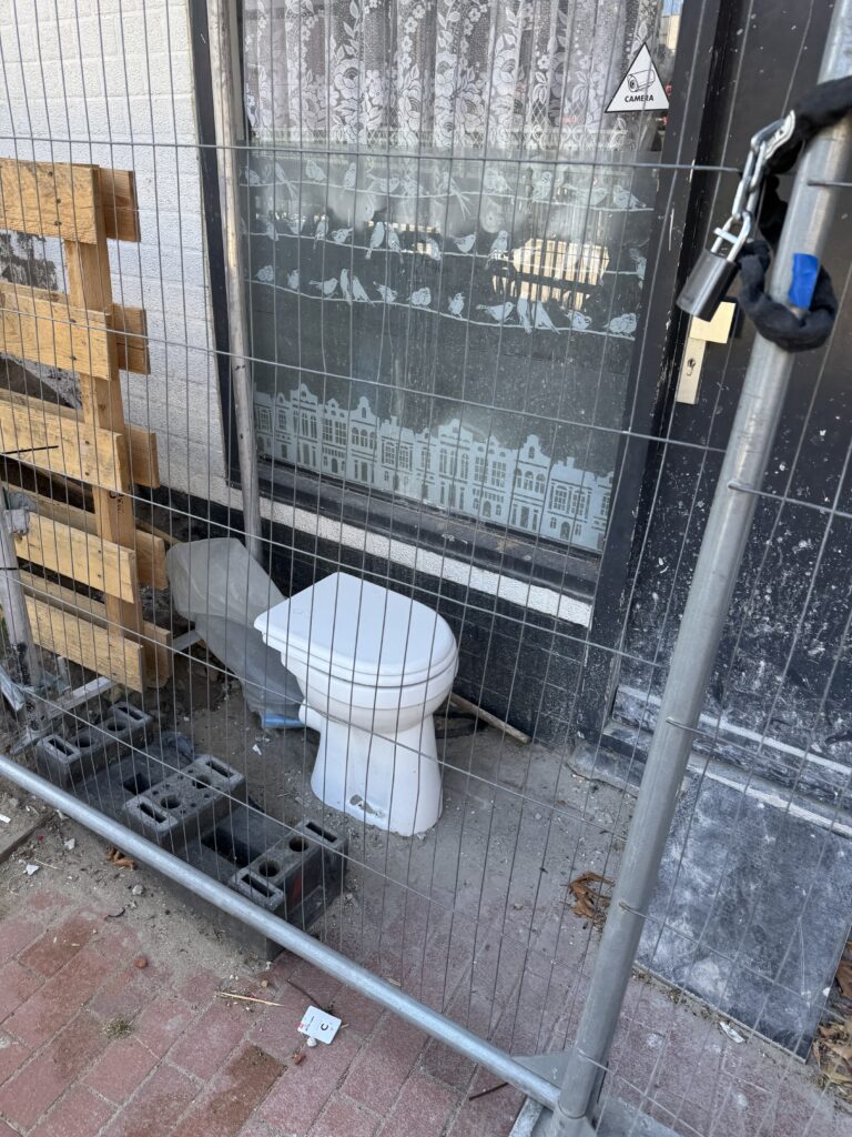 Een toilet dat op de stoep naast een huis staat, met een sticker met de tekst 'camera'